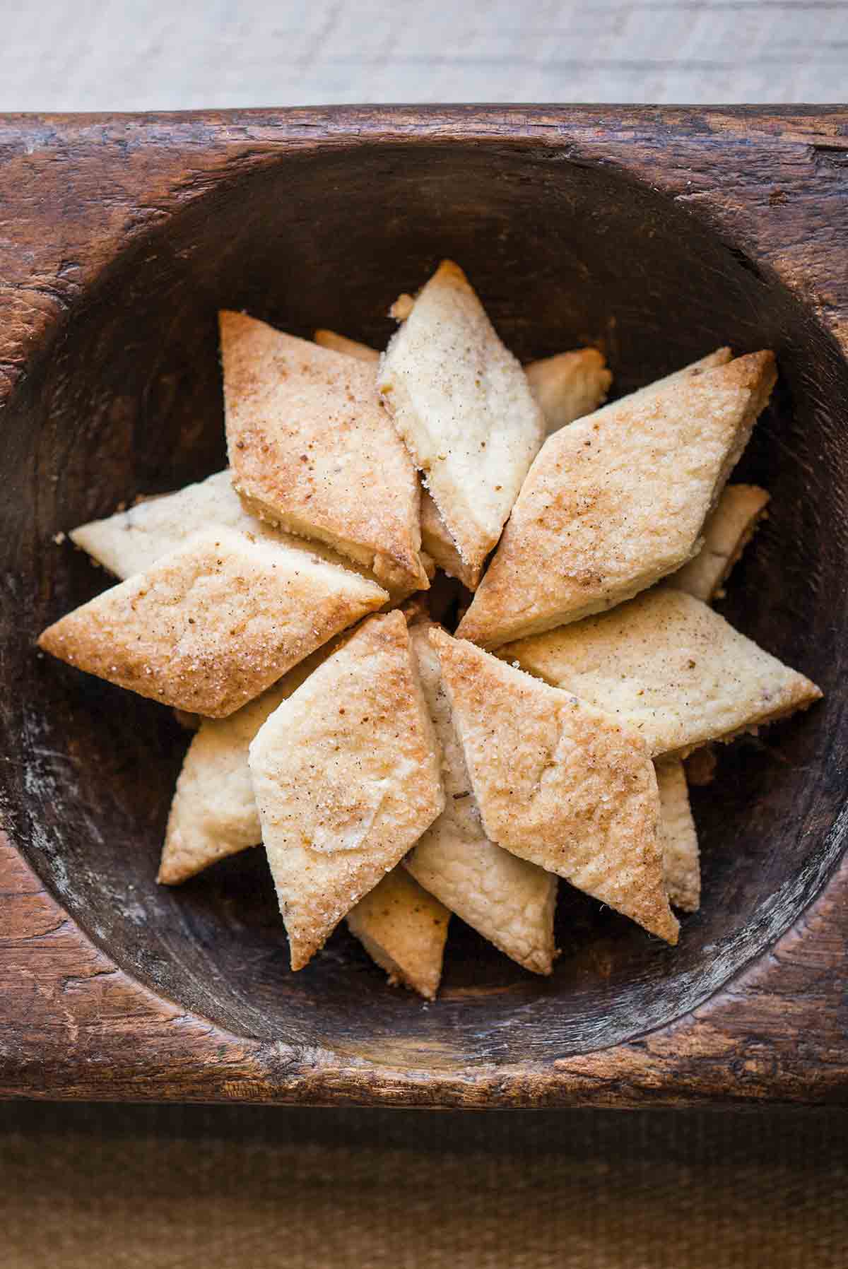 A pile of diamond-shaped biscochitos in a wooden bowl.