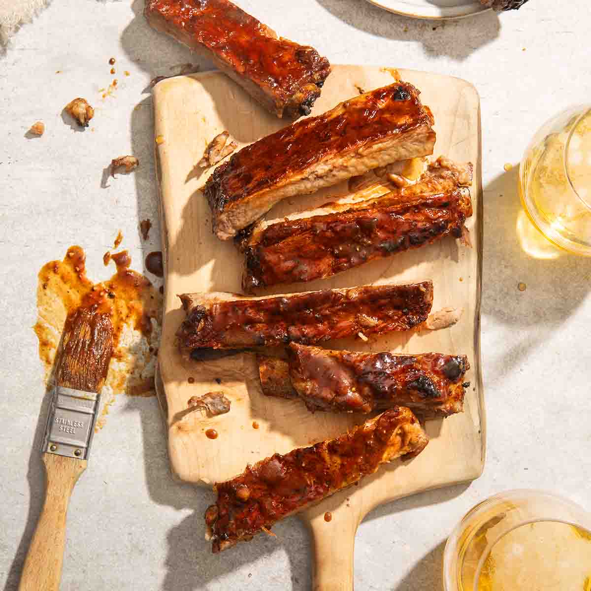 Close up of 6 pork ribs slathered with barbecue sauce with two glasses of beer on the side.