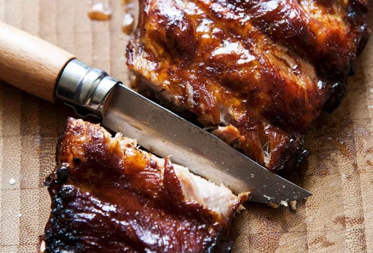 A slab of glazed ribs with a knife cutting between two ribs