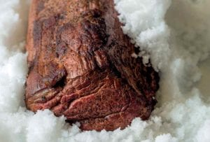 A cooked medium-rare salt-crusted beef tenderloin sitting in a pan of salt