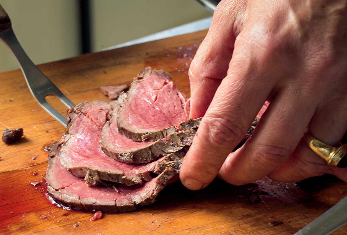 A medium-rare salt-crusted beef tenderloin being sliced on a cutting board