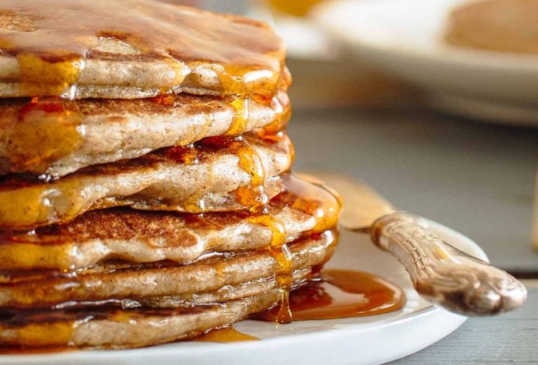 A stack of buckwheat pancakes drizzled with maple syrup on a white plate.