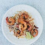 A white plate topped with sauteed shrimp, rice, and lime wedges.