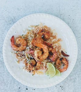 A white plate topped with sautéed shrimp, rice, and lime wedges.