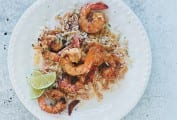 A white plate topped with sauteed shrimp, rice, and lime wedges.