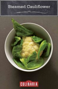 A head of steamed cauliflower in a white bowl on a gray surface.