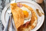 A thin pancake filled with ham and an egg on a white plate, along with a fork and knife.