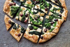 A broccoli rabe pizza cut into squares on a grey background.