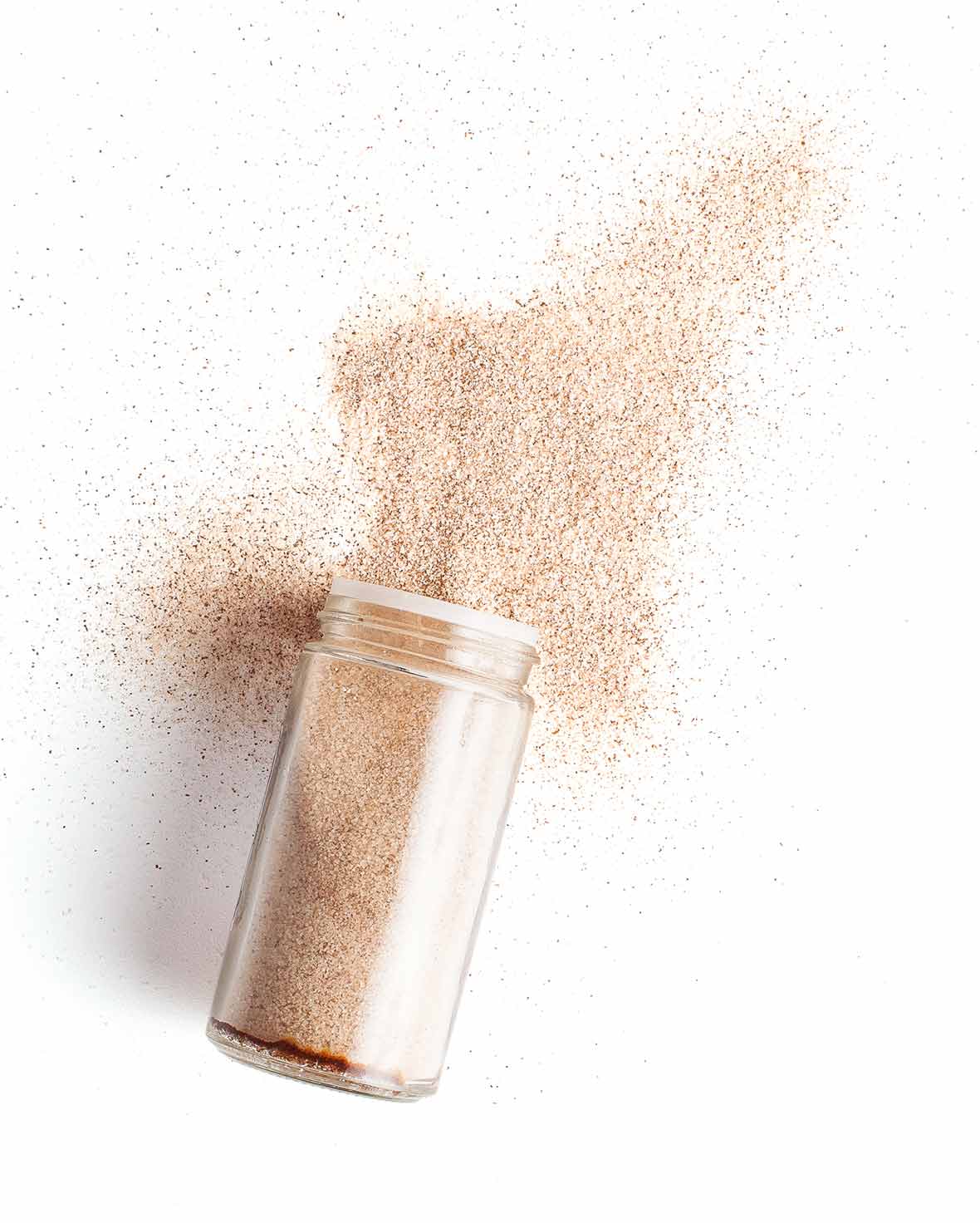 A glass spice jar filled with cinnamon sugar, lying on its side with some cinnamon sugar poured out.