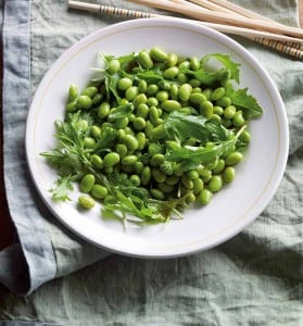 A white bowl filled with edamame salad sitting on a grey linen napkin with chopsticks on the side.