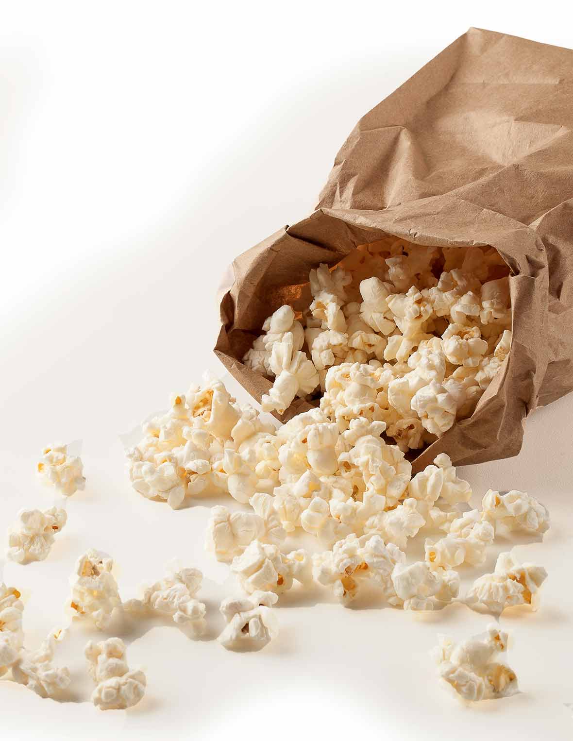 A brown paper bag with popped microwave popcorn spilling out of it.
