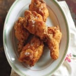 An oval plate with four pieces of Southern fried chicken wings.