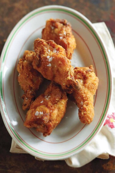 An oval plate with four pieces of Southern fried chicken wings.