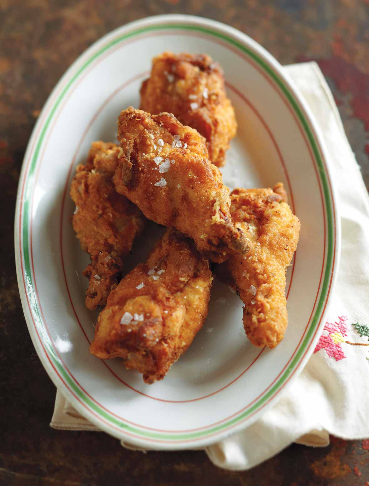 An oval plate with four pieces of Southern fried chicken wings.