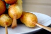 Five corn dogs with sticks on a plate