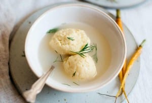 Two gluten free matzo balls in a bowl of broth garnished with dill.