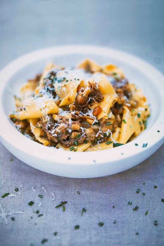 A white bowl filled with pappardelle pasta with meat sauce sprinkled with chopped rosemary.