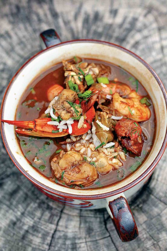 Seafood gumbo in a two-handled bowl on a piece of wood.
