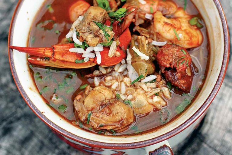 Seafood gumbo in a two-handled bowl on a piece of wood.