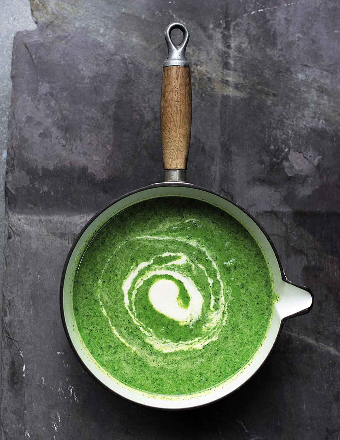 A saucepan filled with green soup, with a swirl of cashew cream in the center.