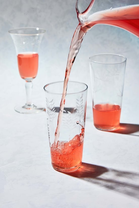 Pink rhubarb vodka streaming from a pitcher into an etched highball glass with ice.