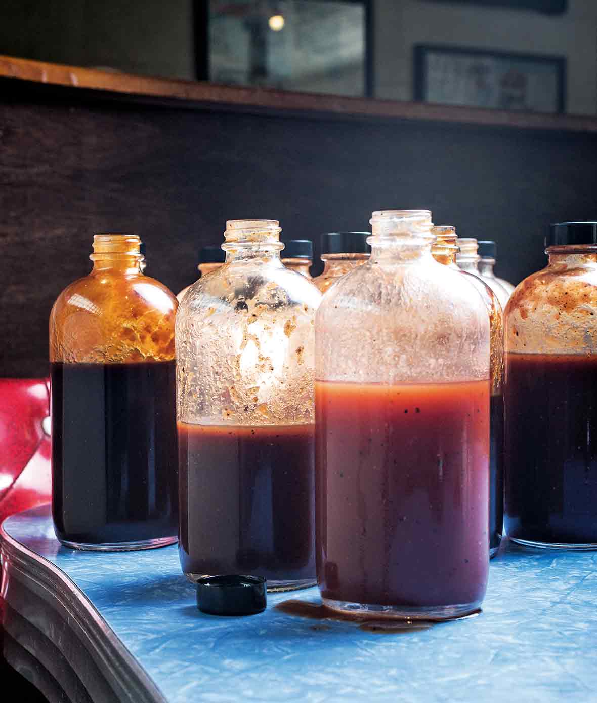 Several open glass bottles of barbecue sauces, including a vinegar barbecue sauce.