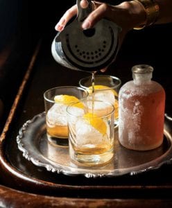 A tray with three old-fashioned cocktails, with a frosted decanter nearby.