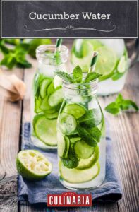 Two small glass bottles filled with cucumber water, cucumber slices, lime slices and mint on a wooden table.