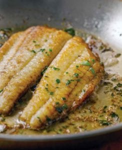 Two fillets of flounder in a lemon butter sauce in a skillet topped with chopped parsley