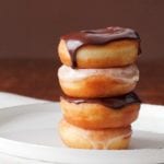 Four glazed doughnuts stacked on top of each other, two with chocolate glaze, 2 with vanilla glaze