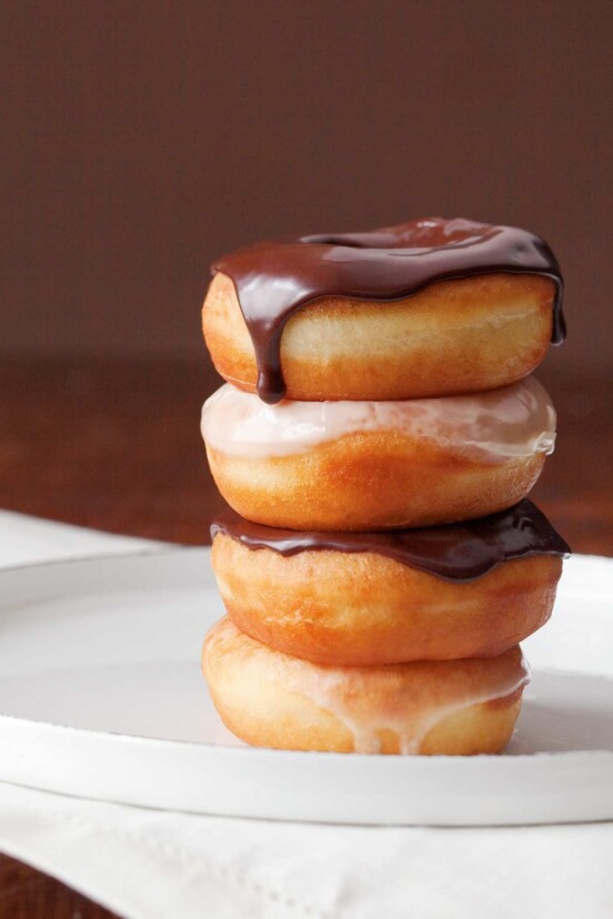Four glazed doughnuts stacked on top of each other, two with chocolate glaze, 2 with vanilla glaze