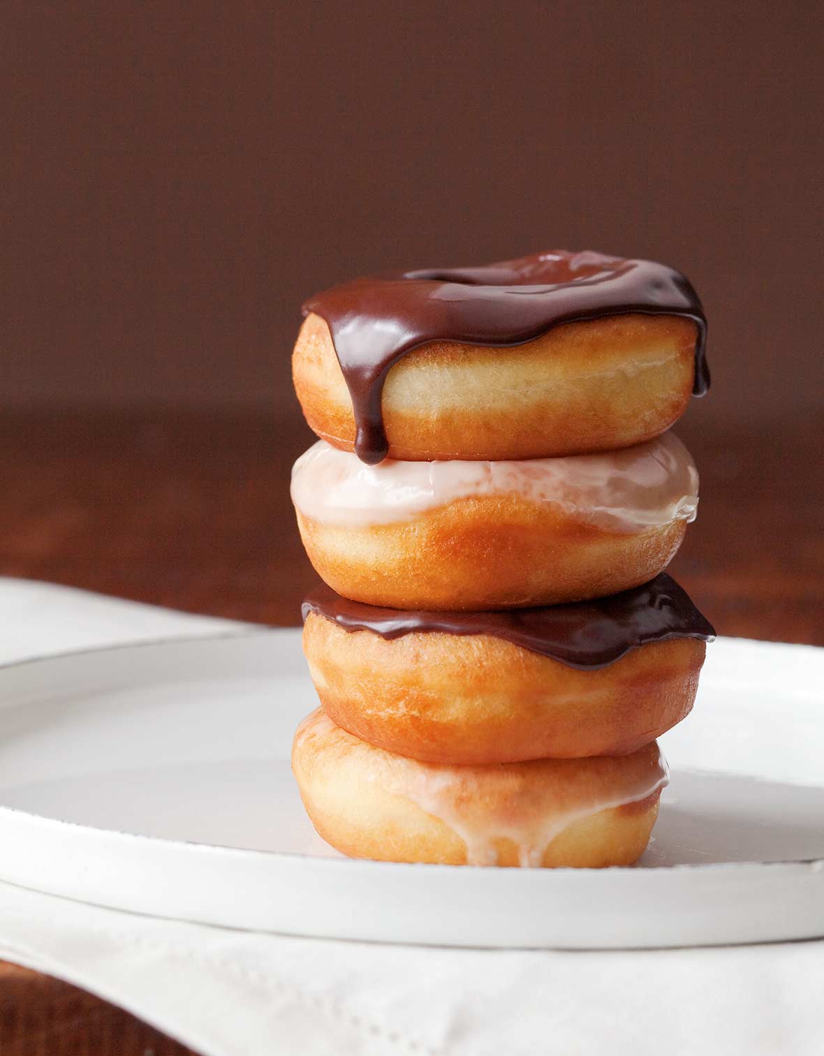 Four glazed doughnuts stacked on top of each other, two with chocolate glaze, 2 with vanilla glaze