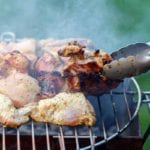 Pieces of grilled chicken with balsamic vinaigrette cooking on a grill, being turned with a pair of tongs.
