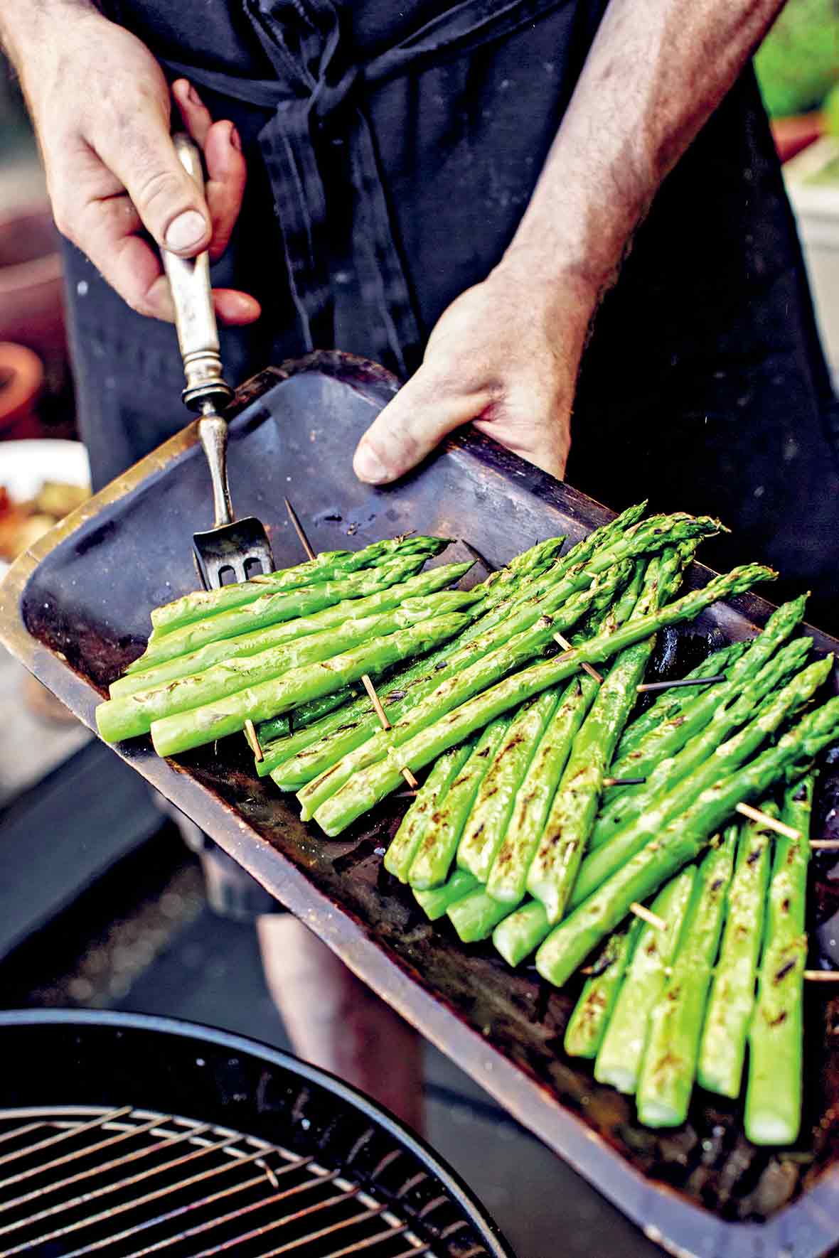 A cook demonstrating how to grill asparagus with several rafts of asparagus spears connected with wooden skewers.