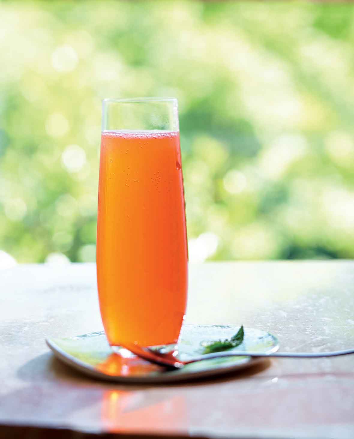 A tall glass of fruit shrub sitting on a napkin with a long spoon next to it.