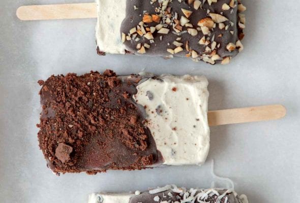 Three homemade ice cream bars, coated with chocolate and sprinkled with almonds, coconut, and chocolate crumbs.