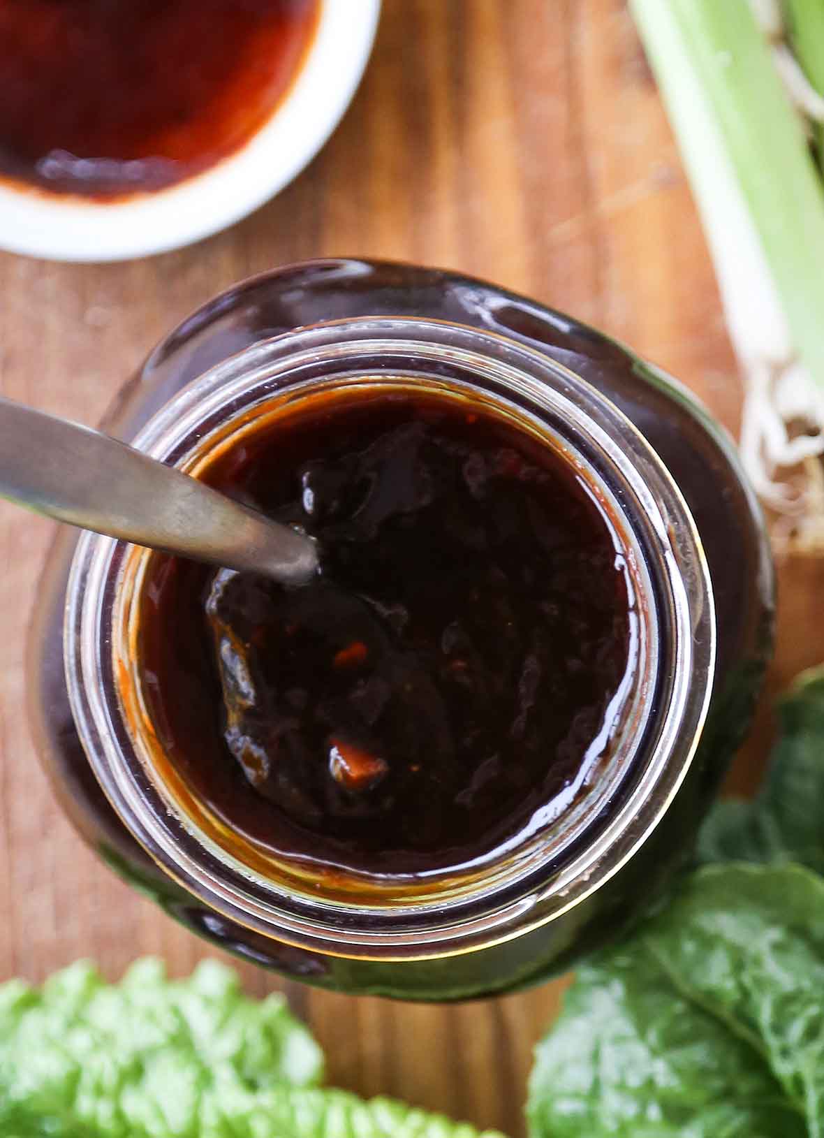 A glass jar filled with Korean barbecue sauce, with some greens beside it.