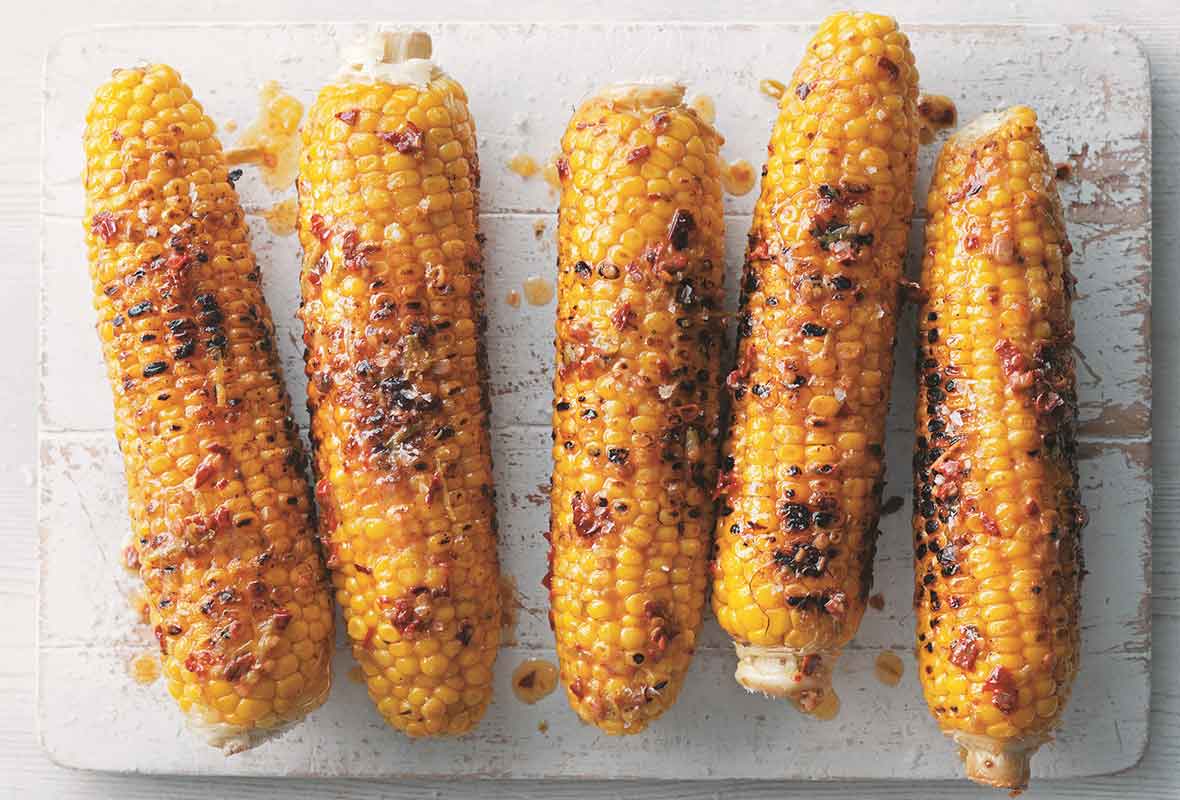 Five ears of Mexican corn on the cob on a white wooden board.
