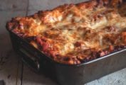 A metal baking dish filled with lasagna bolognese on a wooden surface.