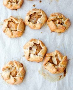 Seven rosemary apple hand tarts on a sheet of parchment.