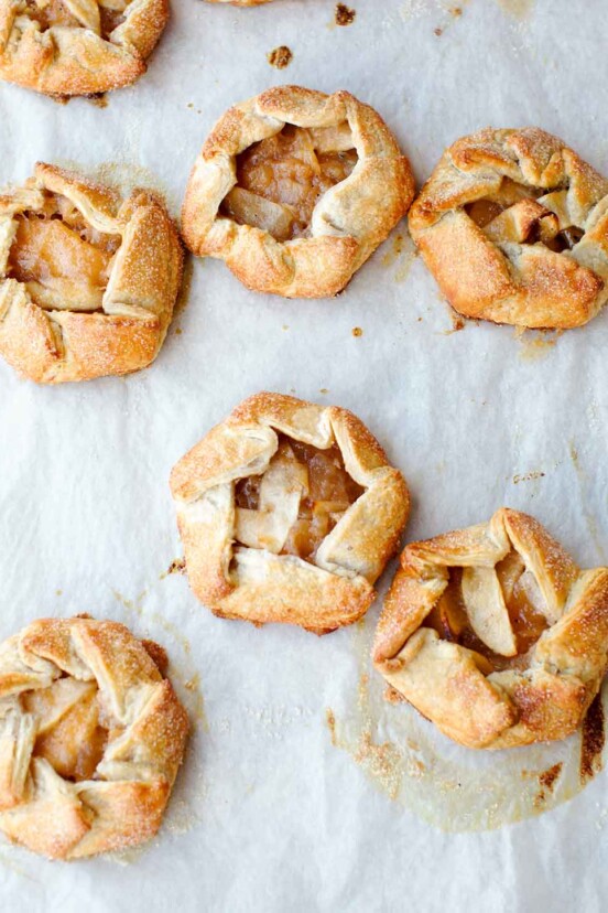 Seven rosemary apple hand tarts on a sheet of parchment.