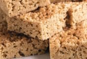 Several squares of pumpkin spice rice krispie treats stacked on a brown and white plate.