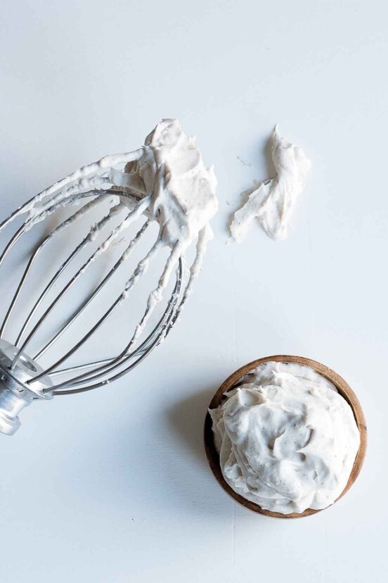 A whisk attachment and a wooden bowl filled with coconut whipped cream.