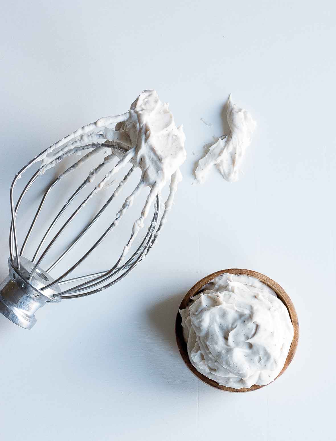 A whisk attachment and a wooden bowl filled with coconut whipped cream.