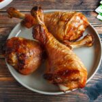 Three smoked turkey legs on a plate with a bowl of coleslaw in the background.