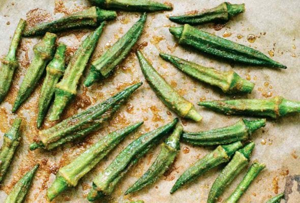 Pieces of roasted okra with spices on a parchment-lined baking sheet.