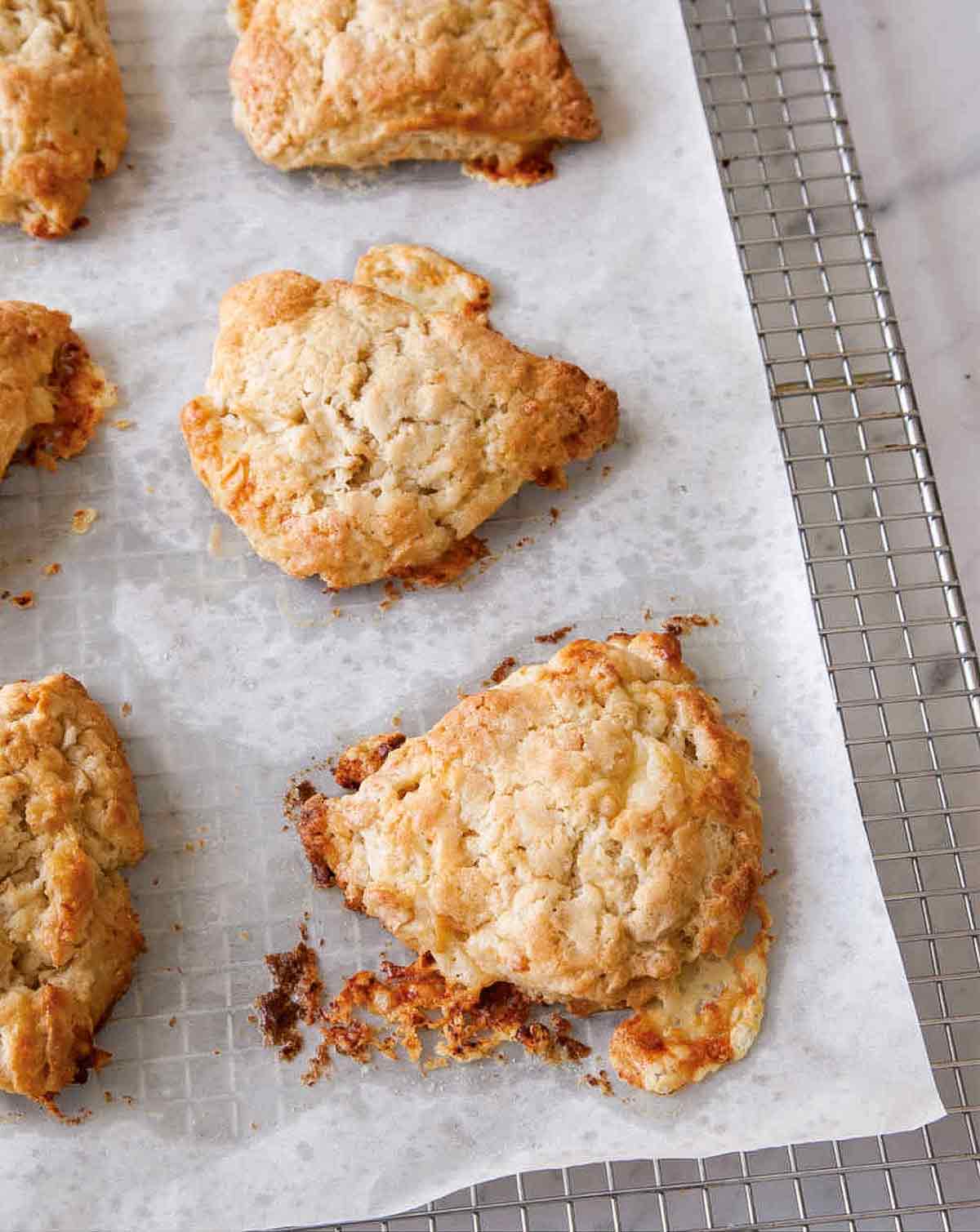 Six apple and white cheddar scones on a piece of parchment on top of a cooling rack.