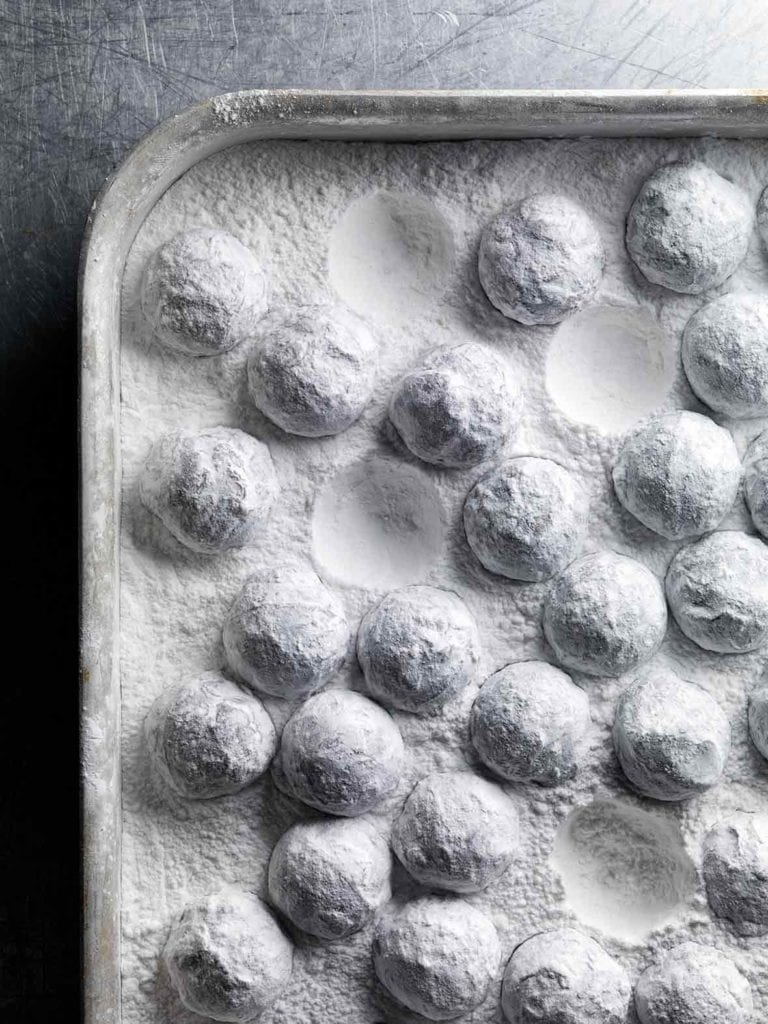 A rimmed sheet pan filled with truffles coated in confectioners' sugar