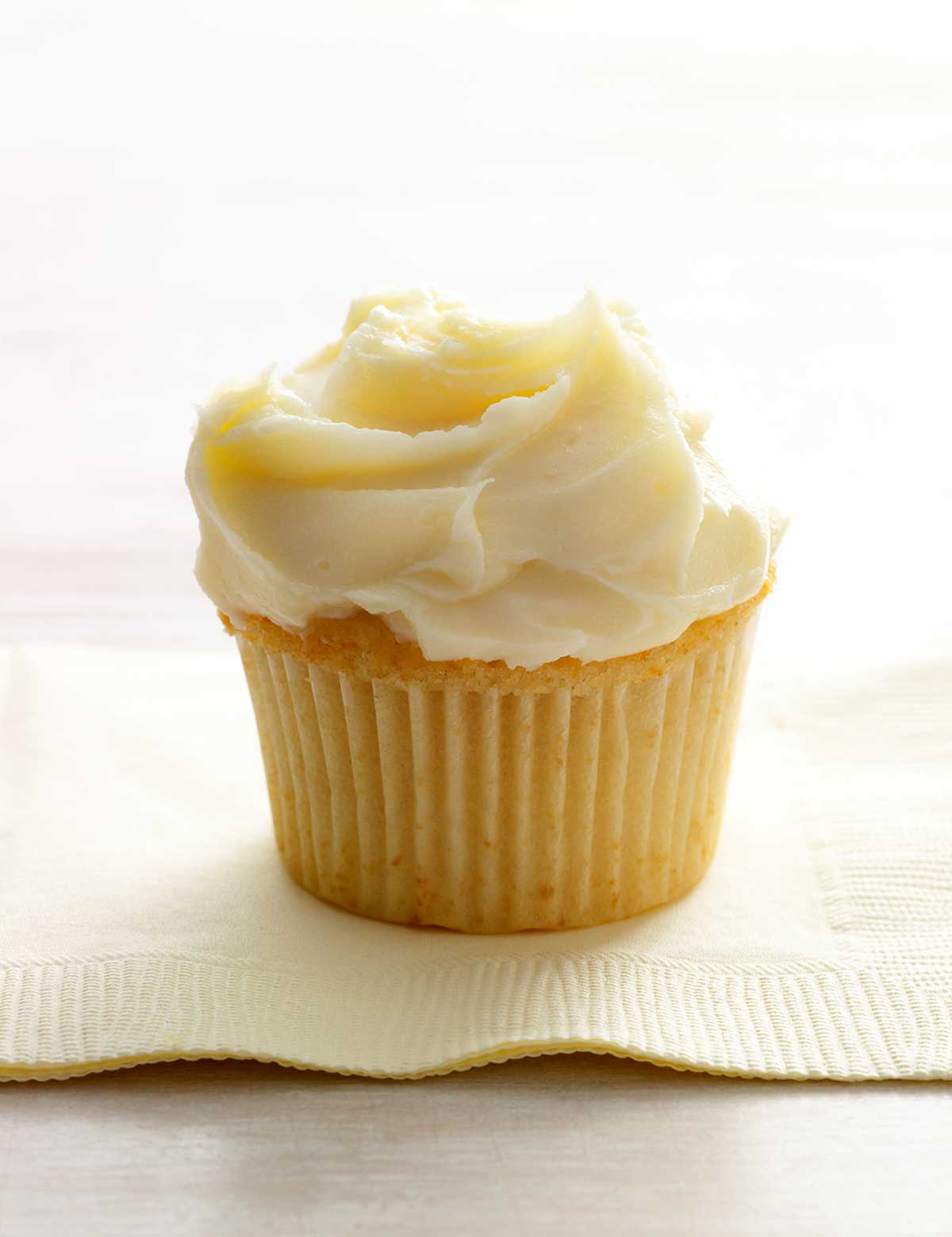 A single white chocolate cupcake, topped with white frosting on a paper napkin.