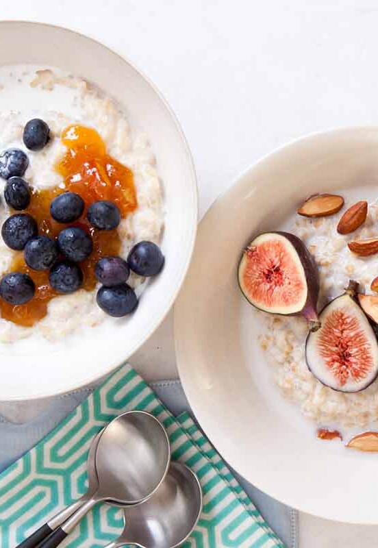Two white bowls filled with porridge; one topped with blueberries and the other with figs and almonds.